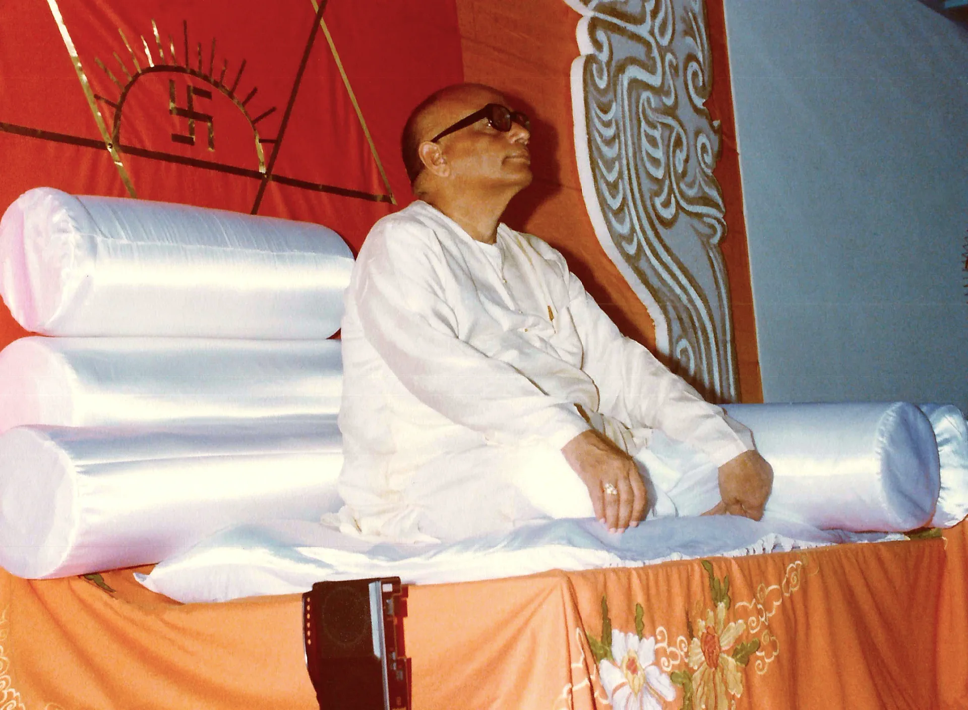 Shrii Shrii Anandamurti seated on a dais with bolsters